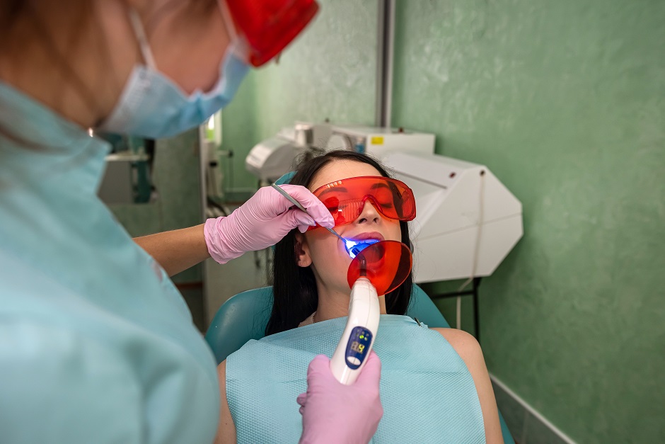 Doctor with lamp and mirror treating patients teeth close up